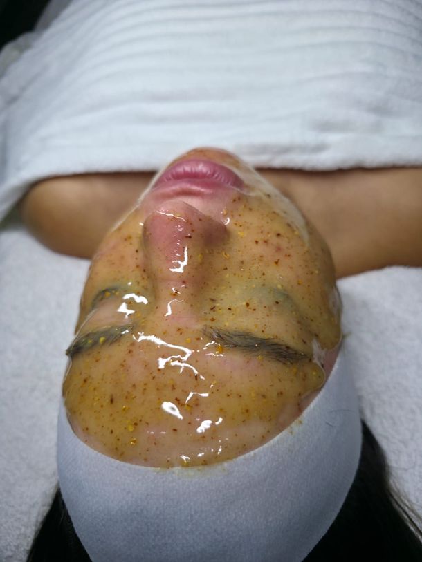 Una persona tumbada en una camilla de spa con una mascarilla facial texturizada de color ámbar aplicada sobre la piel.
