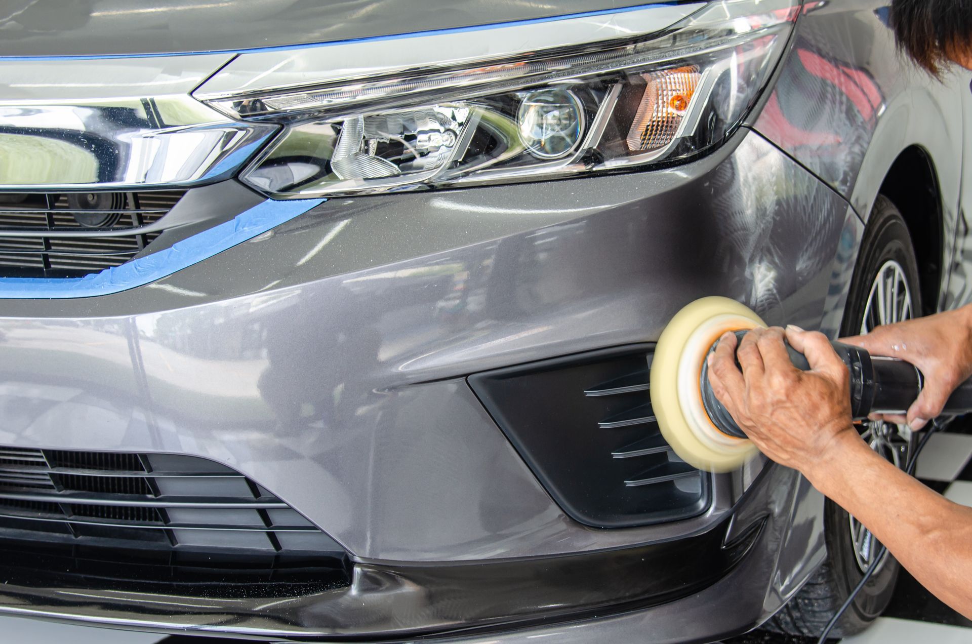 Person polishing a silver car’s front bumper with a buffer in a car wash.