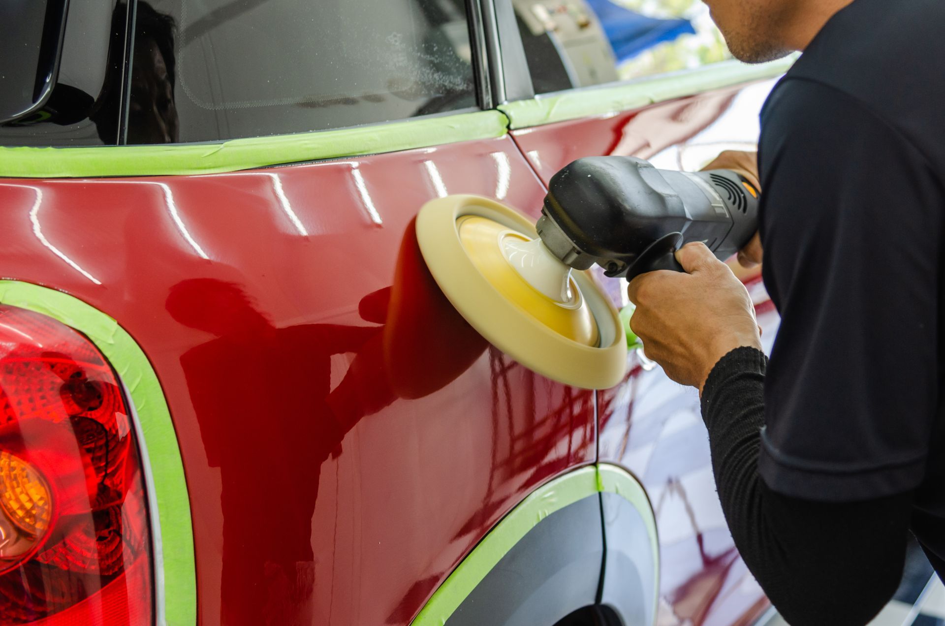 Person using a buffer to polish a red car body panel