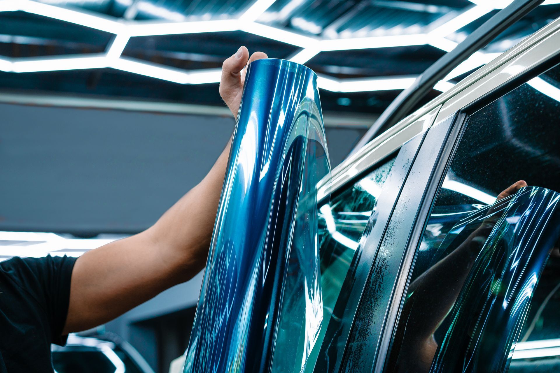 Person placing a blue reflective film on a car window in a modern workshop