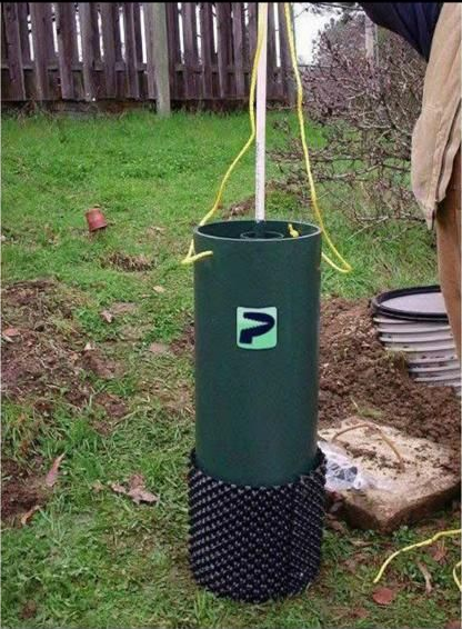 Green well casing with a black base and yellow ropes in a grassy yard.