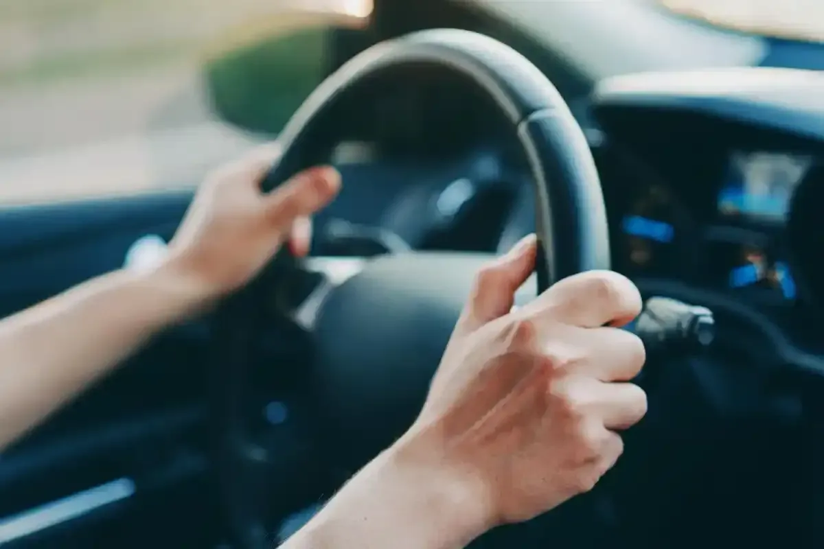 Mani che stringono un volante nero all'interno di un'auto, alla guida.