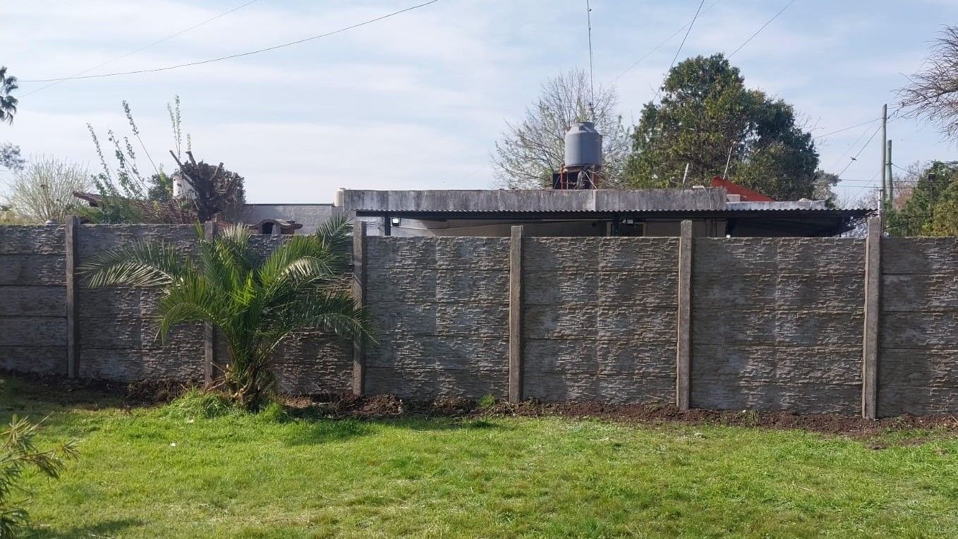 Una valla de hormigón rodea un campo de hierba con una casa al fondo.