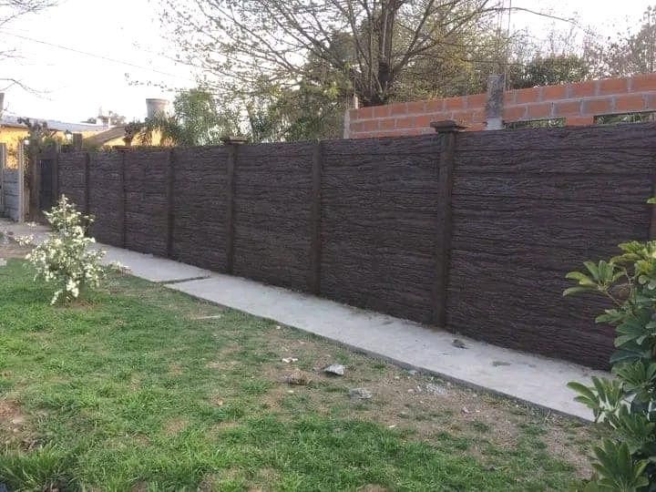Una larga valla de hormigón rodea un exuberante patio verde.