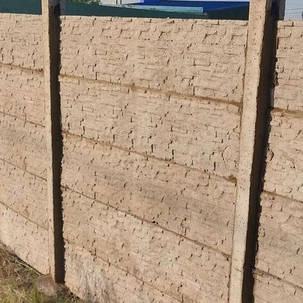 Un primer plano de una valla de hormigón con una casa al fondo.