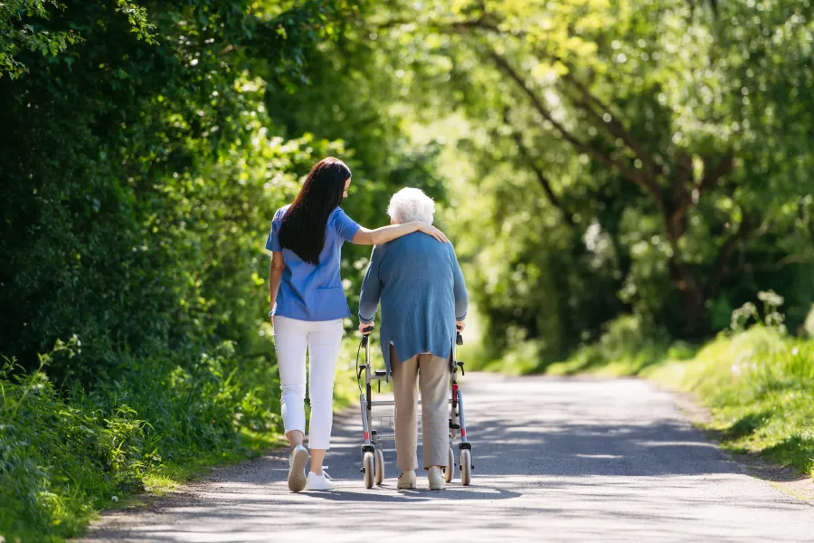 A woman is helping an elderly woman with a walker down a road.