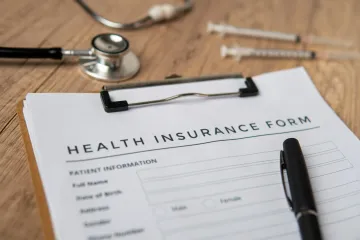 A health insurance form is on a clipboard next to a stethoscope and syringes.