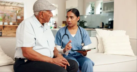 A nurse is sitting on a couch talking to an elderly man.