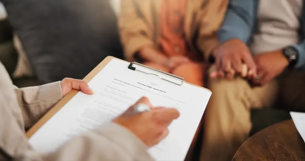 A woman is holding a clipboard in front of a couple sitting on a couch.