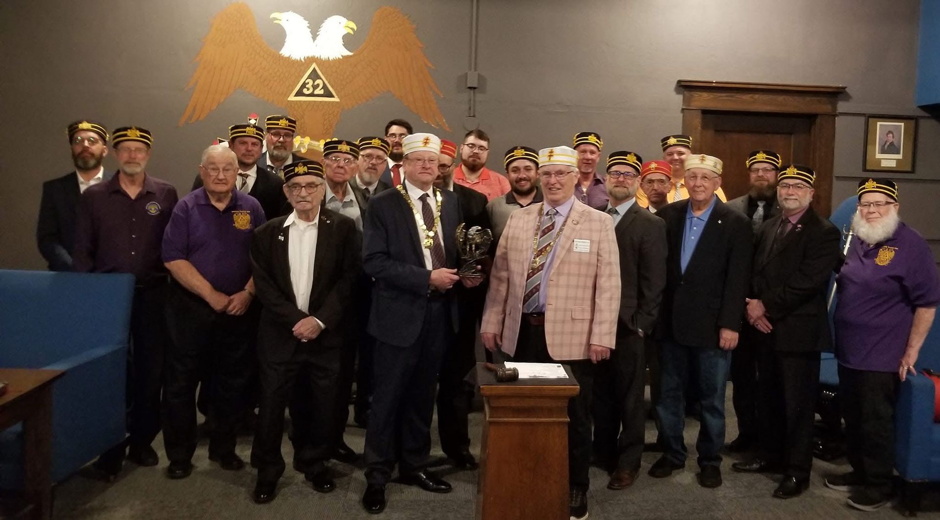 Group of men in suits and hats standing near a podium with a double-headed eagle emblem on the wall.