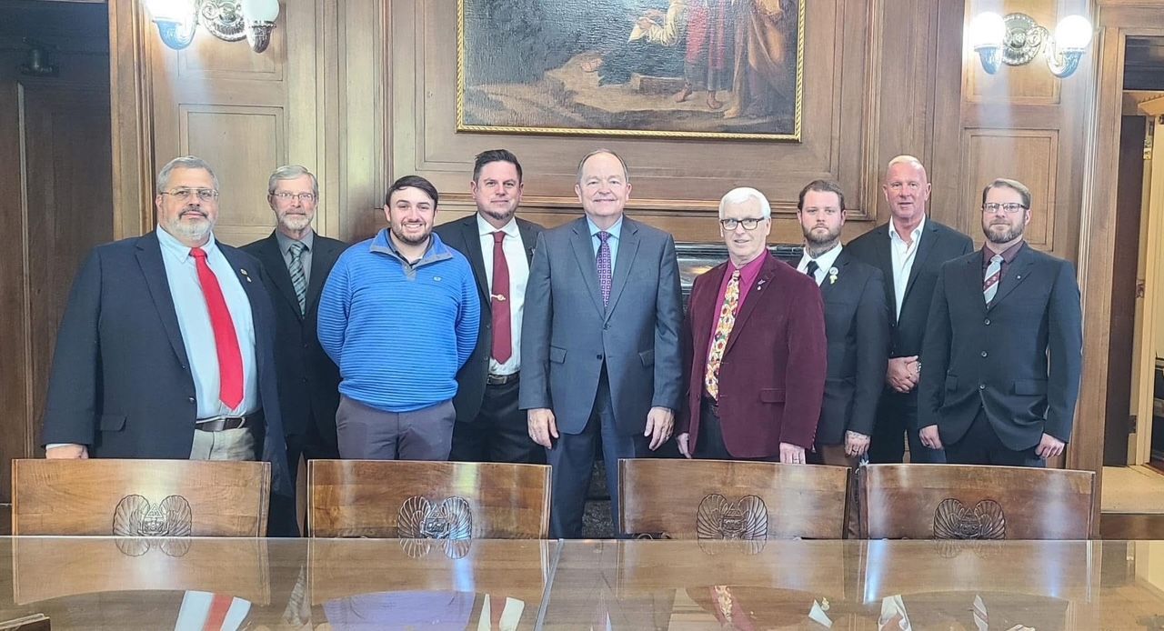 Group of ten men in a formal room, posing behind a long table.