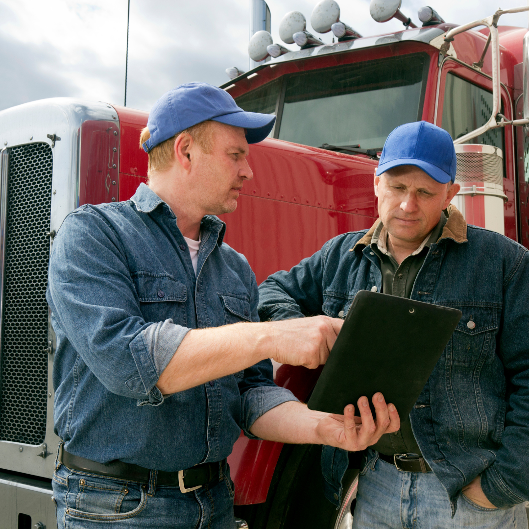 Two men are looking at a clipboard in front of a red truck