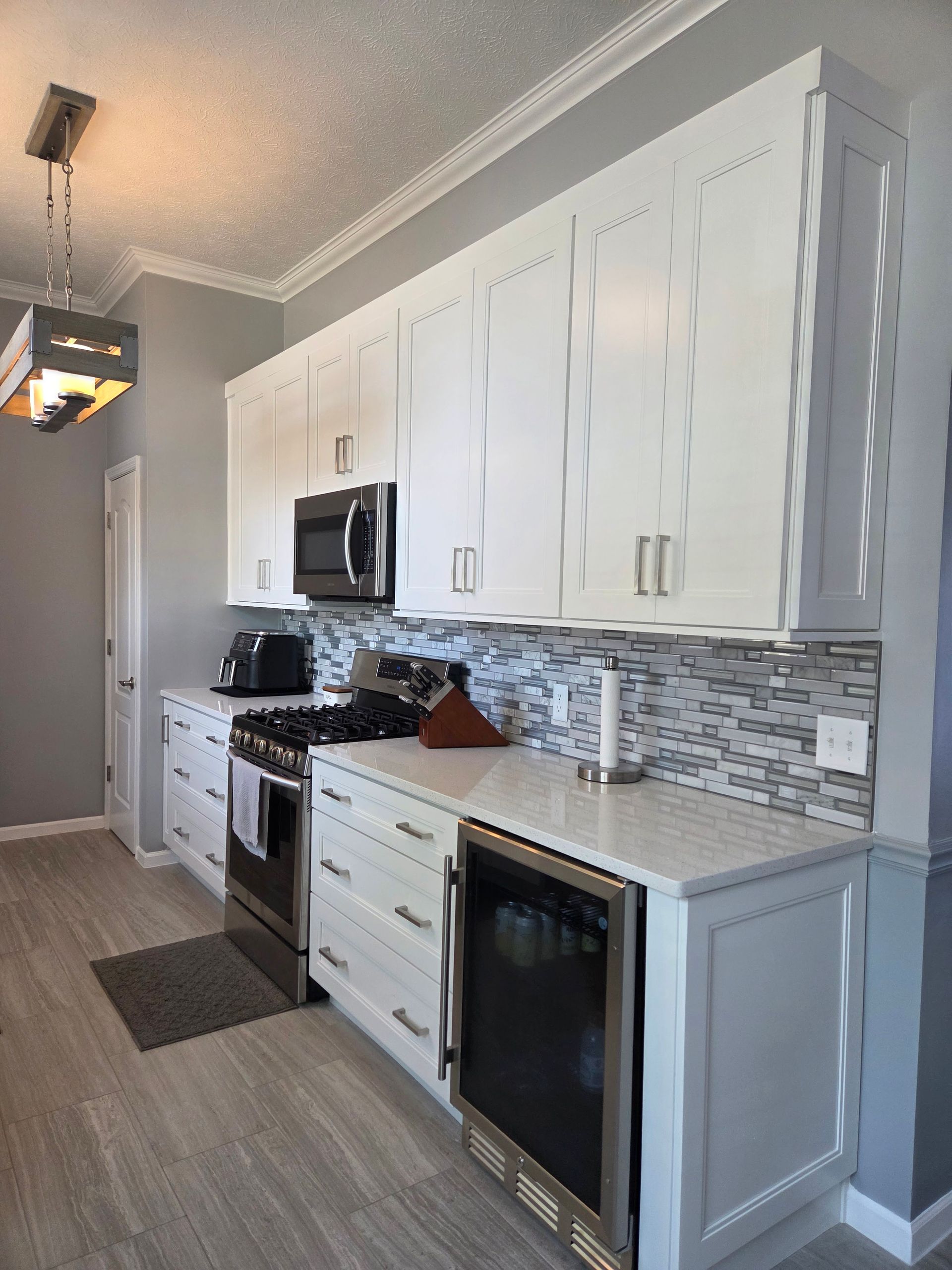 Modern kitchen with white cabinets, stainless appliances, gray mosaic backsplash, and black oven range.