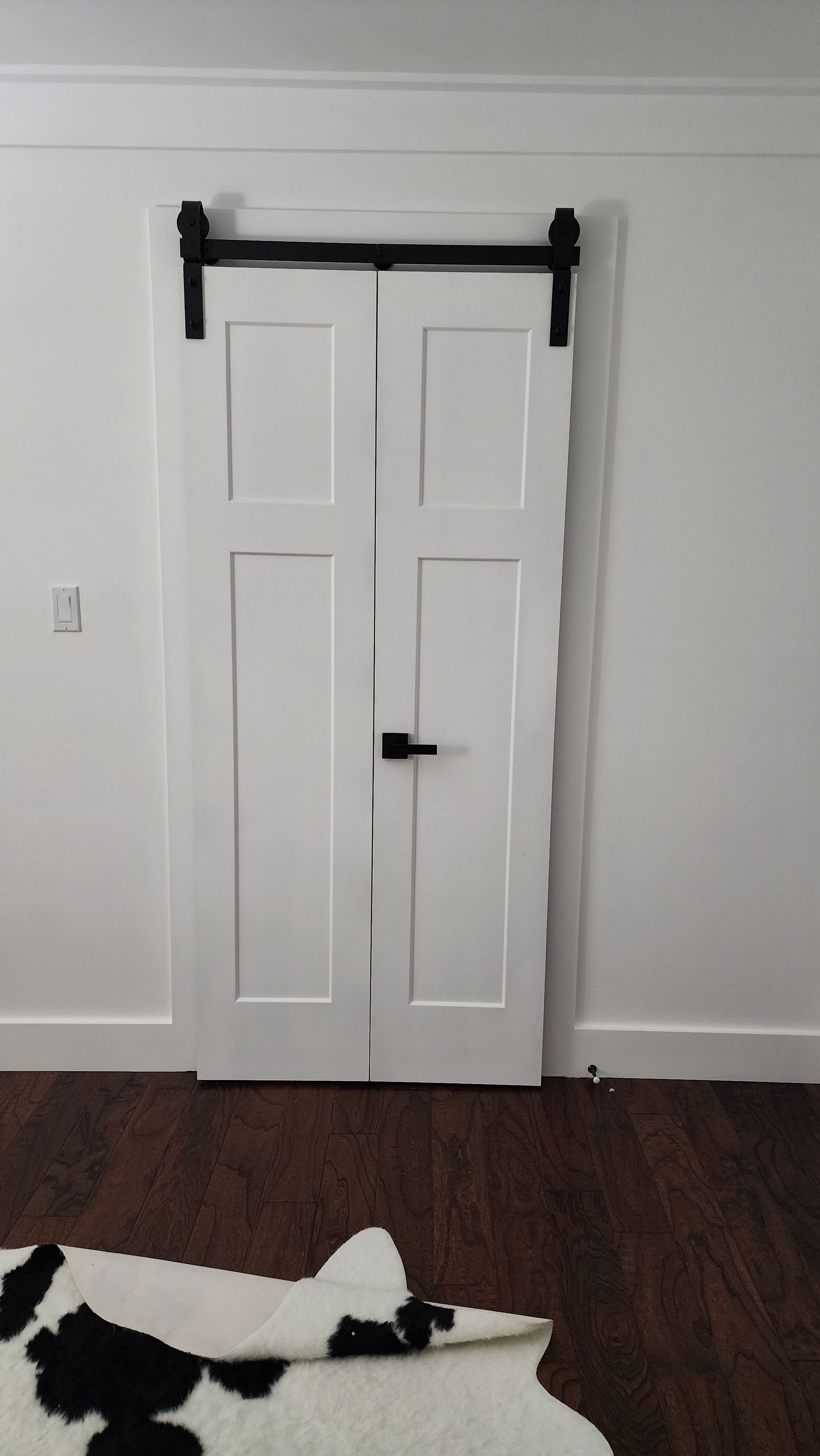 White double barn doors with black hardware in a room with dark wood floor and white walls