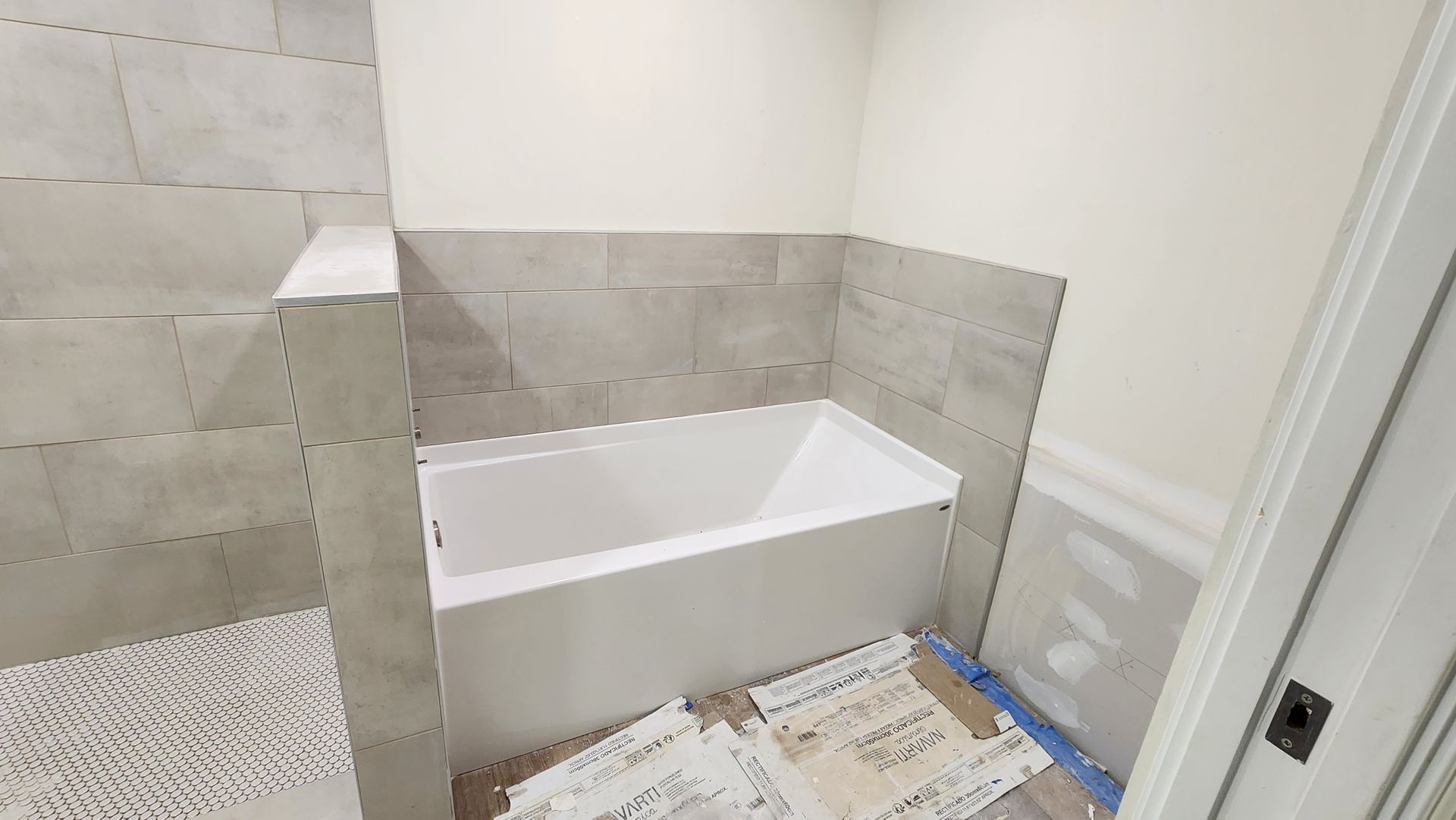 Partially tiled bathroom with a white bathtub and unfinished floor