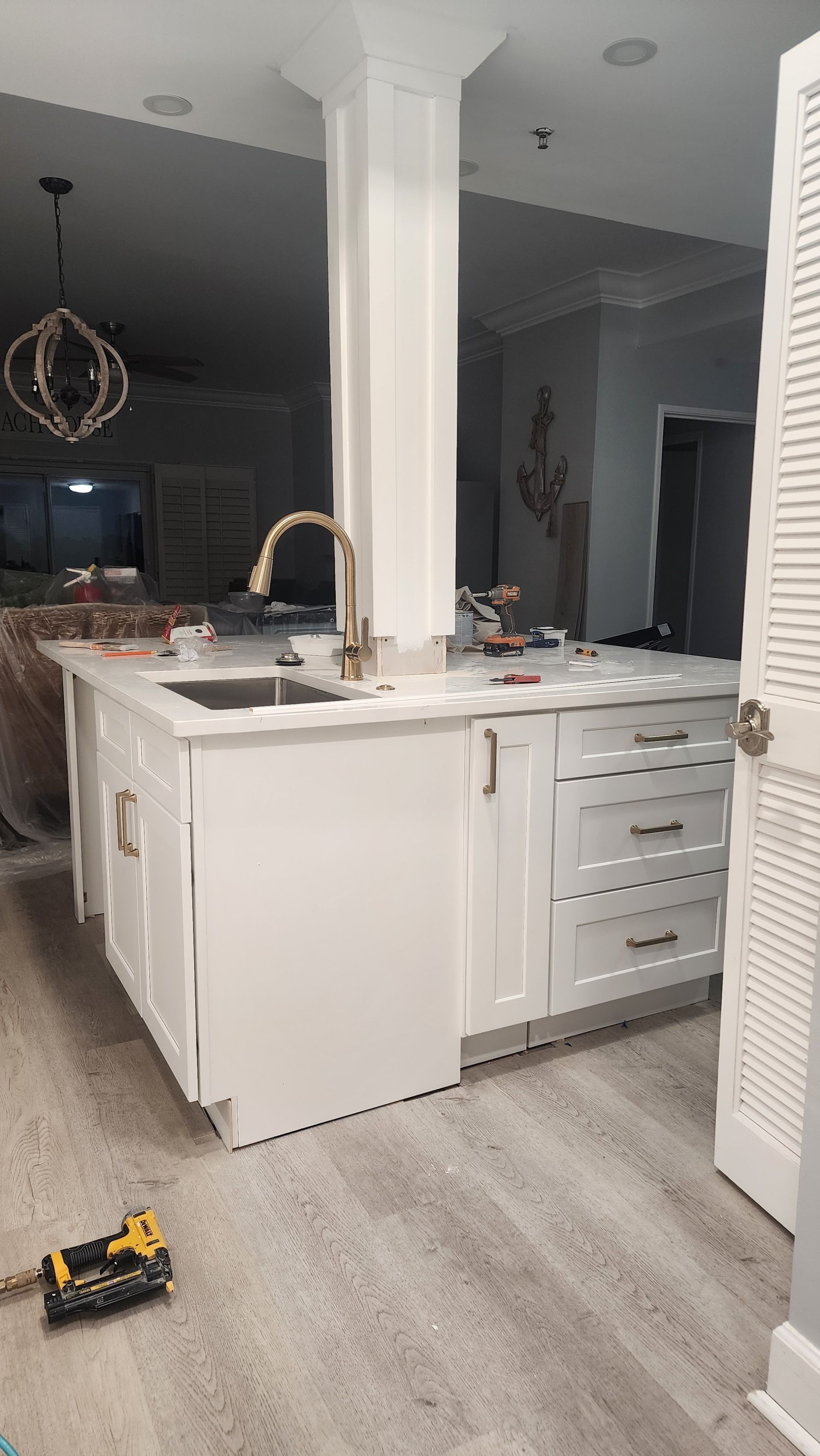 White kitchen island with sink and gold faucet in a modern open-plan home; small toy truck on the floor.