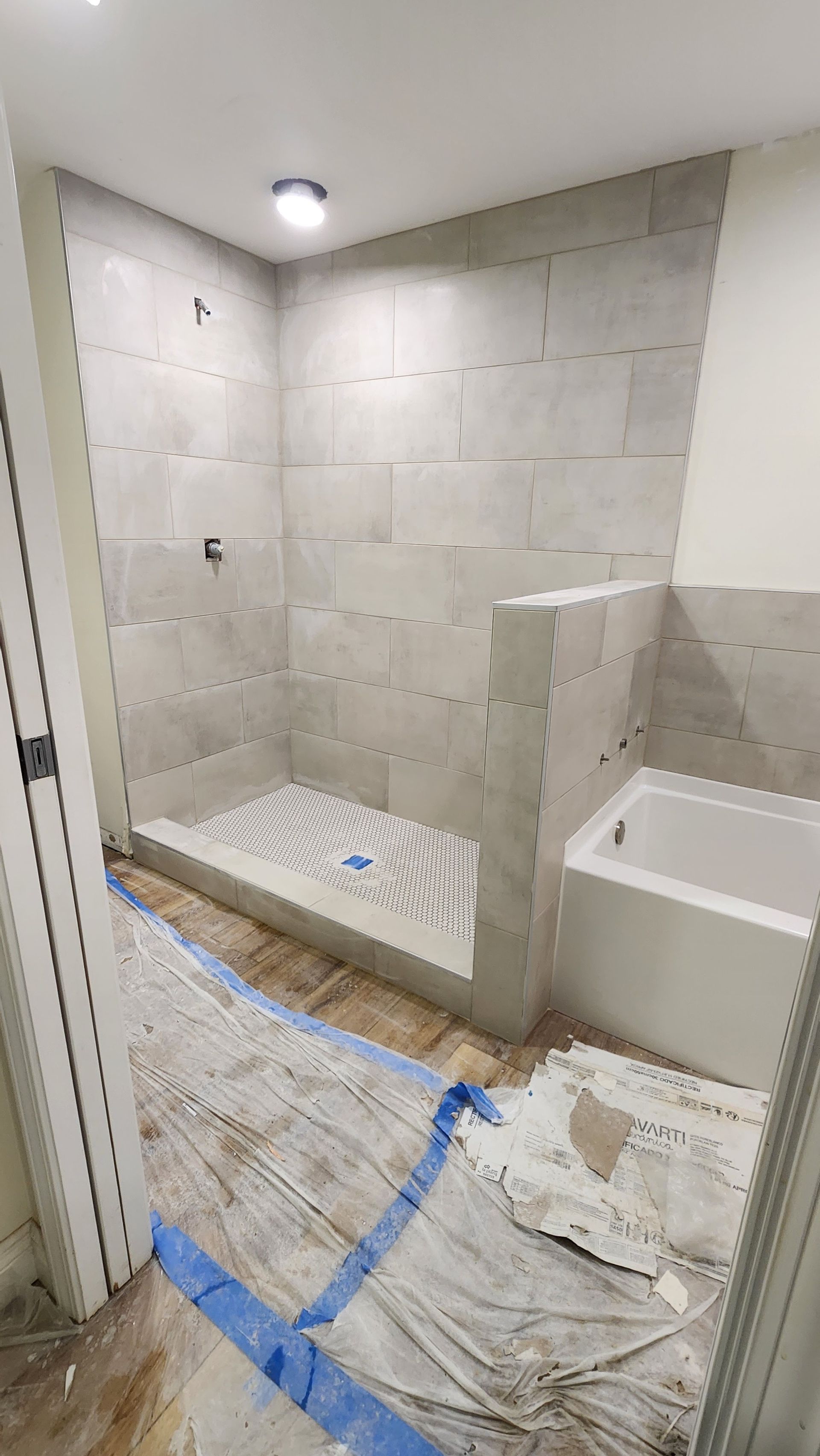 Small tiled bathroom under renovation with shower, vanity sink, and floor protected by drop cloths.