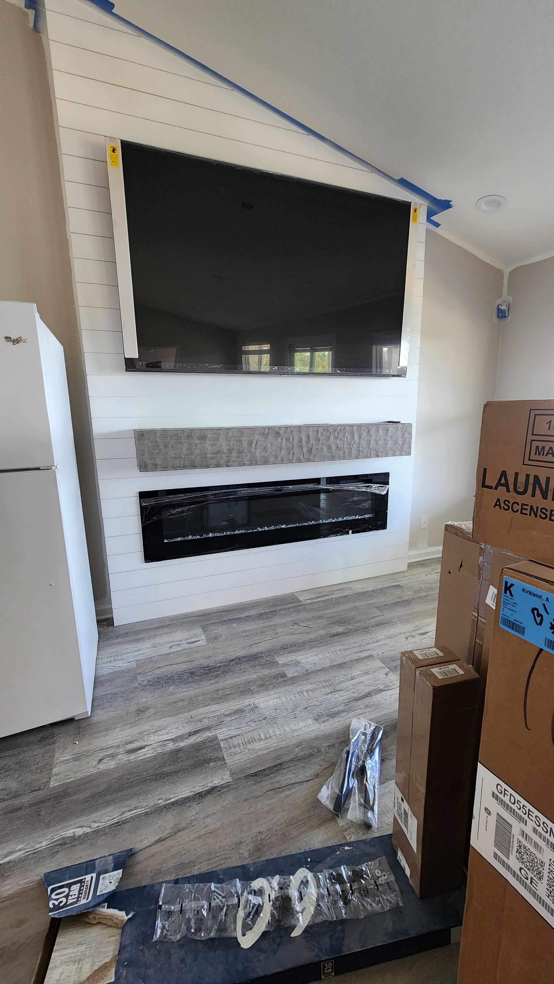 Living room with wall-mounted TV above a fireplace and hardwood floor, with moving boxes in the foreground