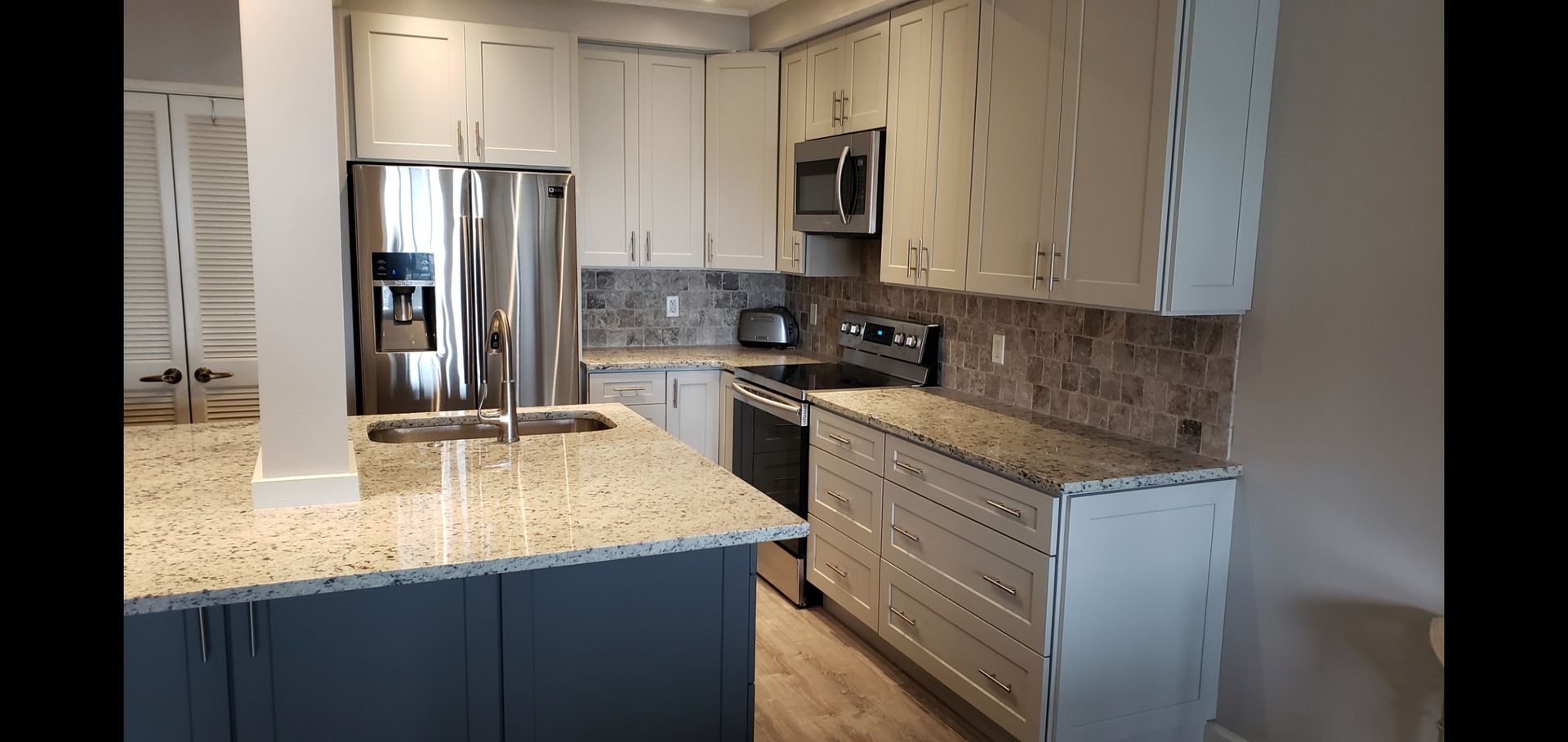 Modern kitchen with granite island, stainless steel appliances, white cabinets, and wood flooring