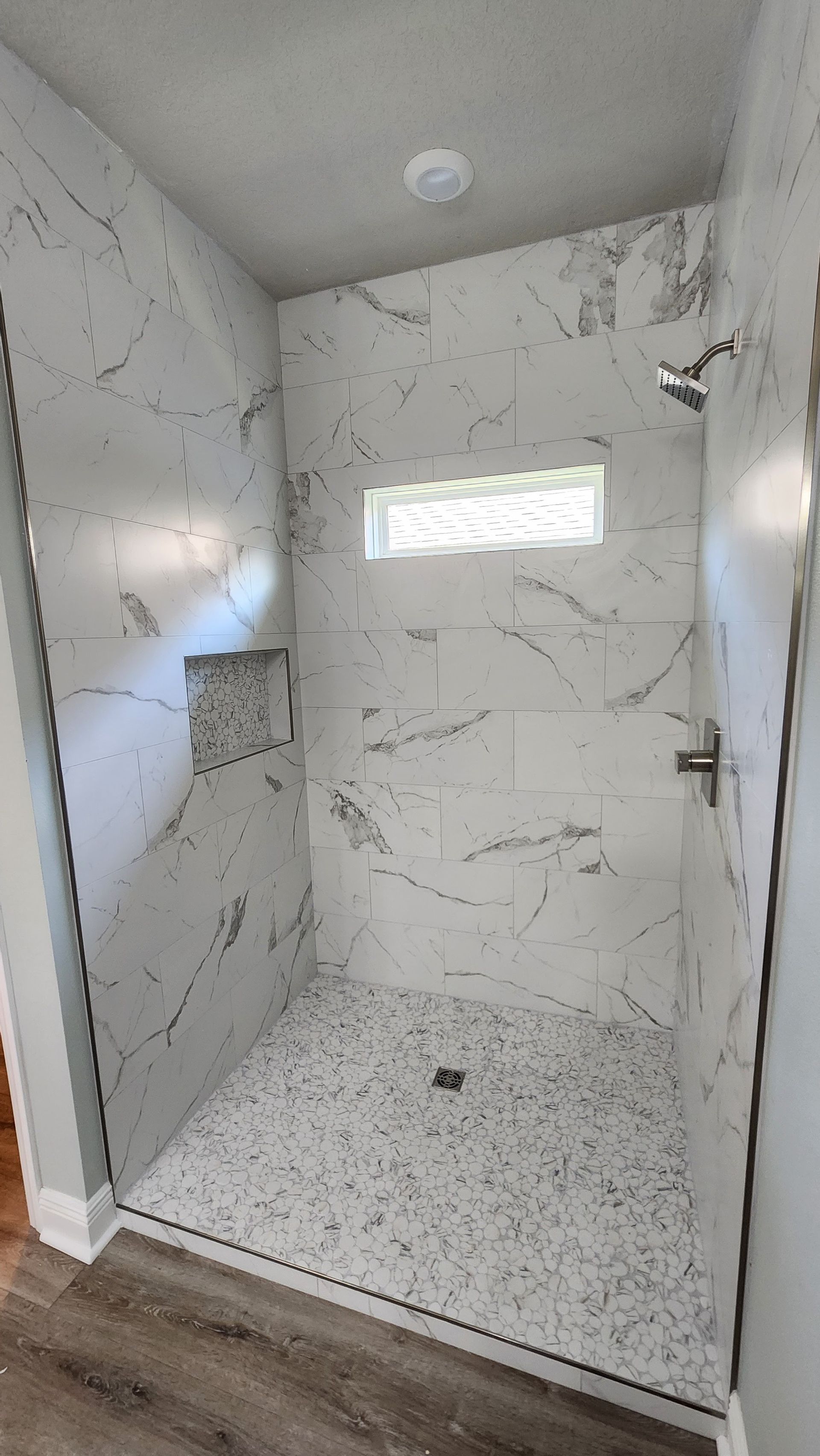 Empty modern tiled shower stall with a small window and glass door.
