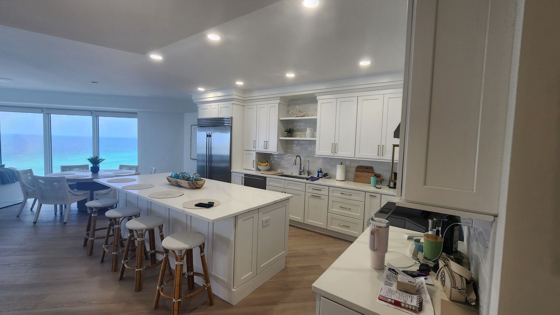 Bright modern kitchen and dining area with white cabinets, island stools, and ocean view beyond sliding doors