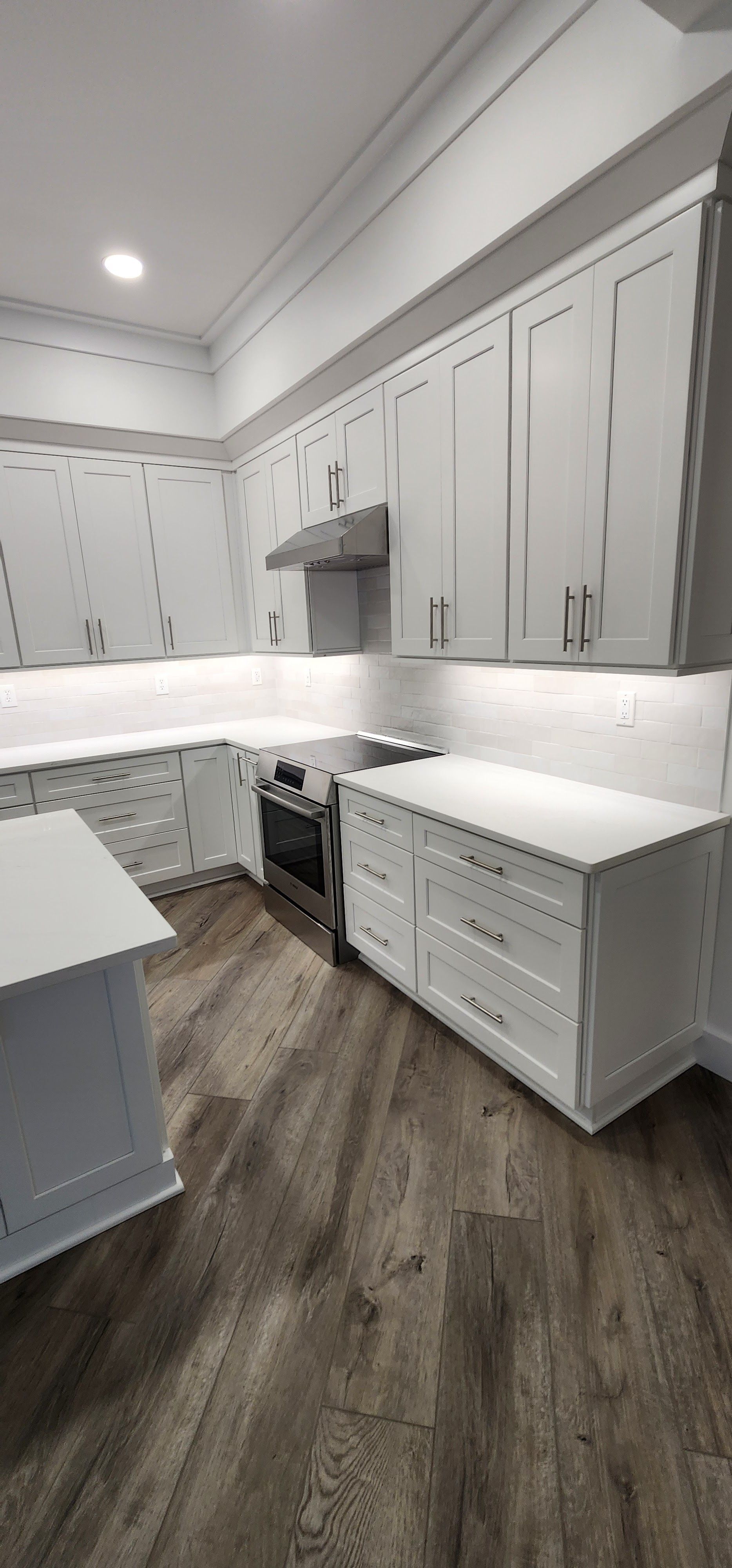 Modern white kitchen with gray cabinets, quartz counters, and wood-look flooring