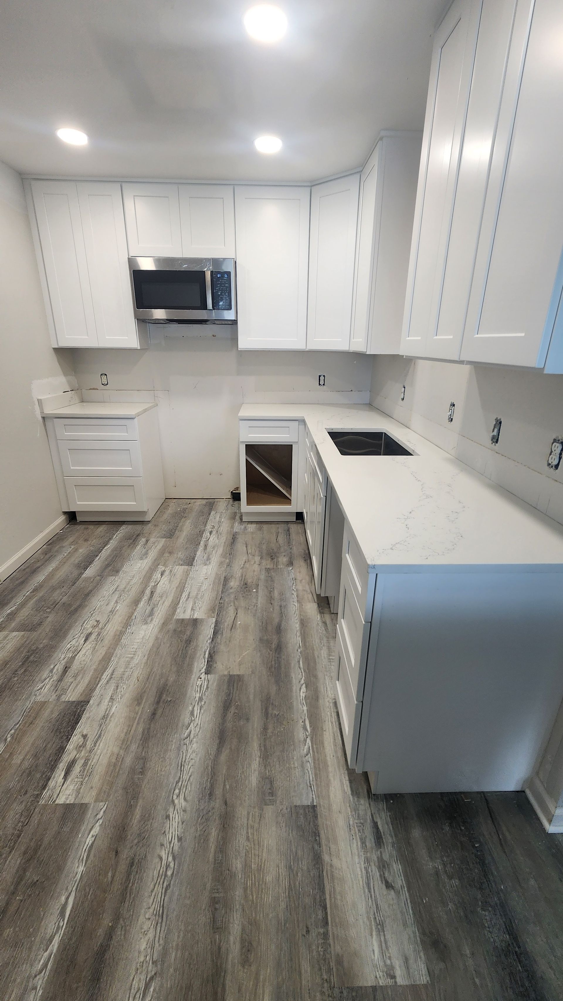 Bright white kitchen with cabinets, stove, sink, and wood-look flooring