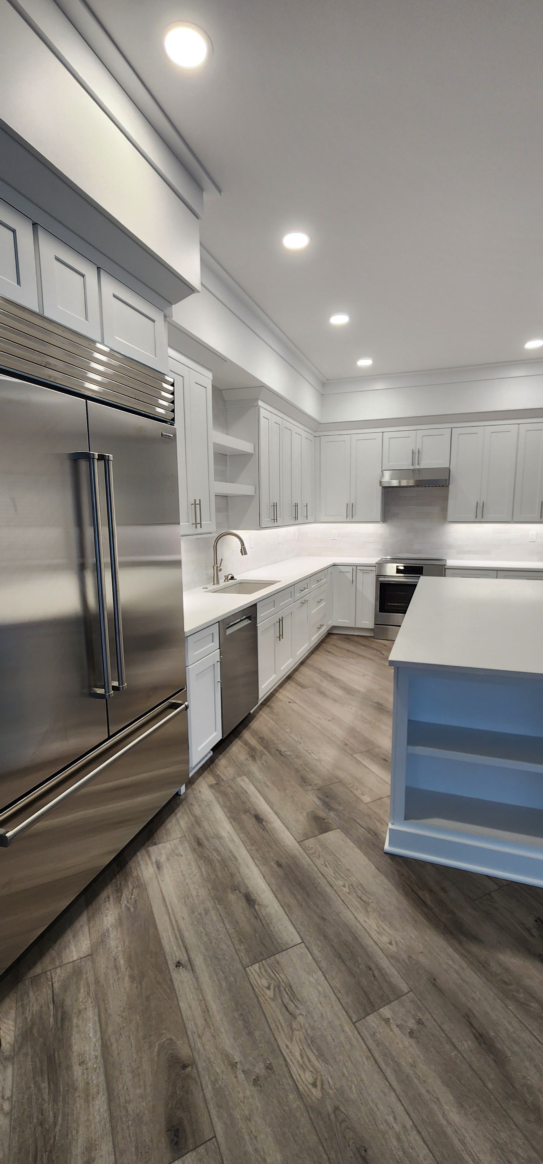 Bright modern kitchen with stainless steel fridge, white cabinets, island, and wood-look floor