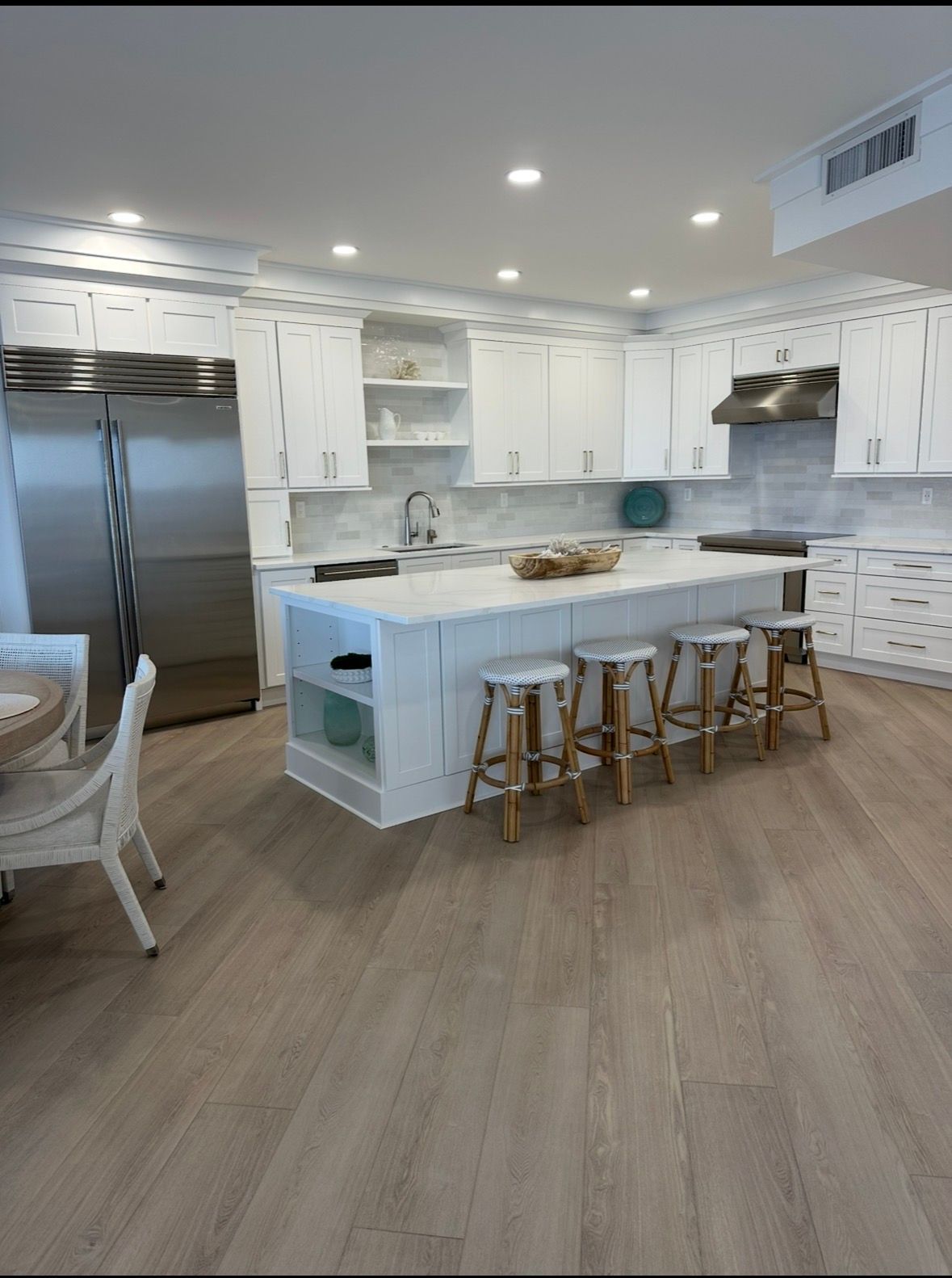 Bright white kitchen with island, stools, stainless steel fridge, and light wood flooring