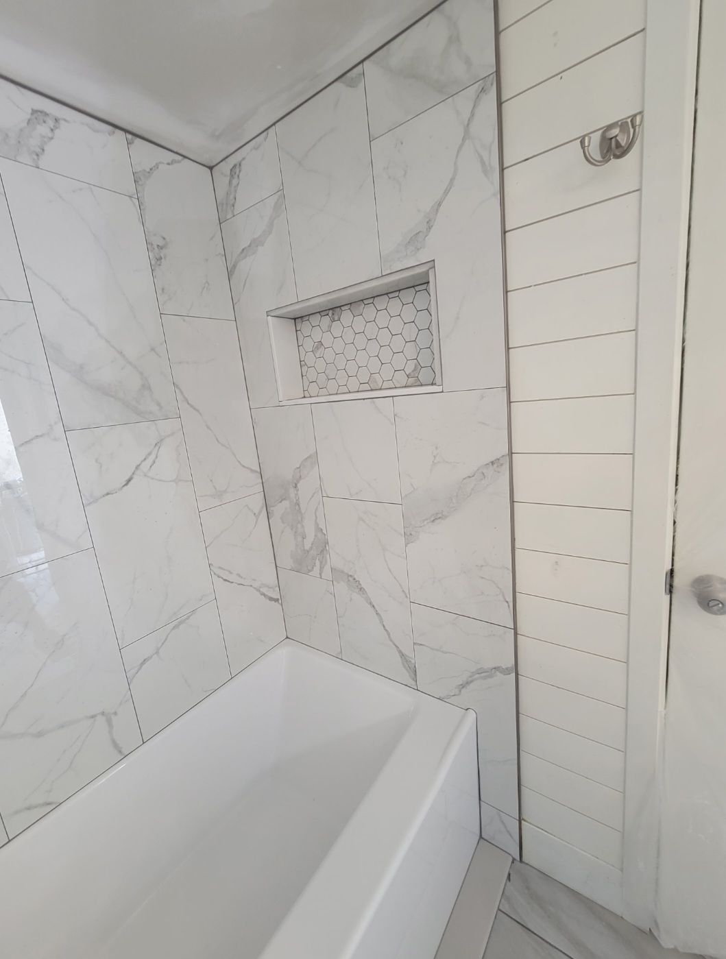 White tiled bathroom with a bathtub and small recessed wall shelf.