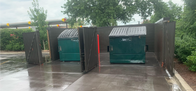 two green dumpsters are sitting next to each other on a wet sidewalk