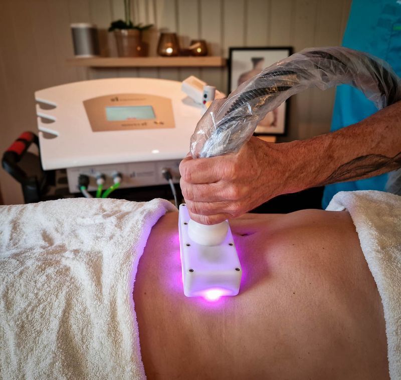 Therapist applying Waves 21 treatment to the lower back using a purple LED handpiece – promoting circulation and recovery.