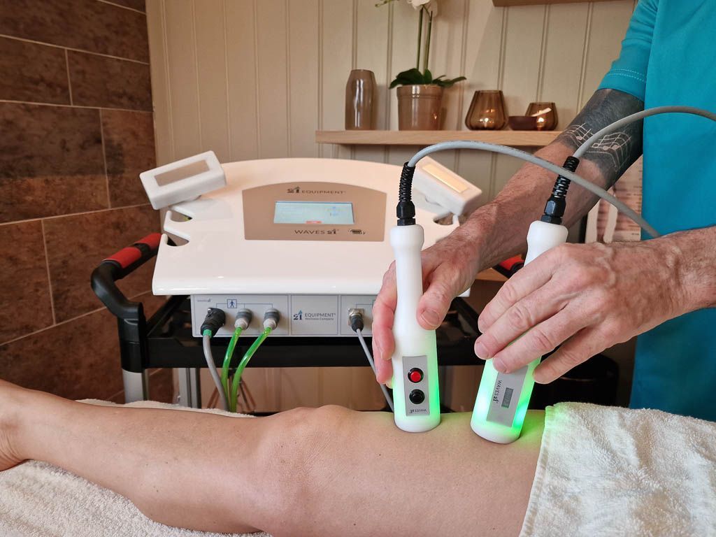 Practitioner using green LED handpieces from the Waves 21 system to treat a client's knee – neuromuscular stimulation in action.