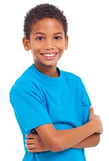 A young boy in a blue shirt is standing with his arms crossed and smiling.
