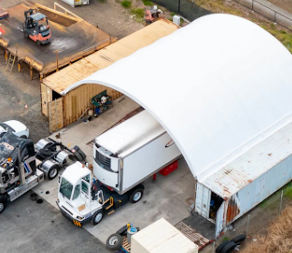 Aerial view of covered storage facility with trucks and equipment parked under protective canopy next to shipping container units