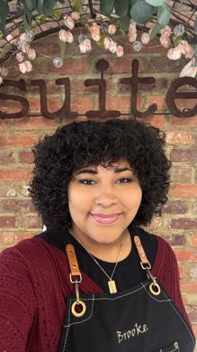 A woman with curly hair is standing in front of a brick wall.
