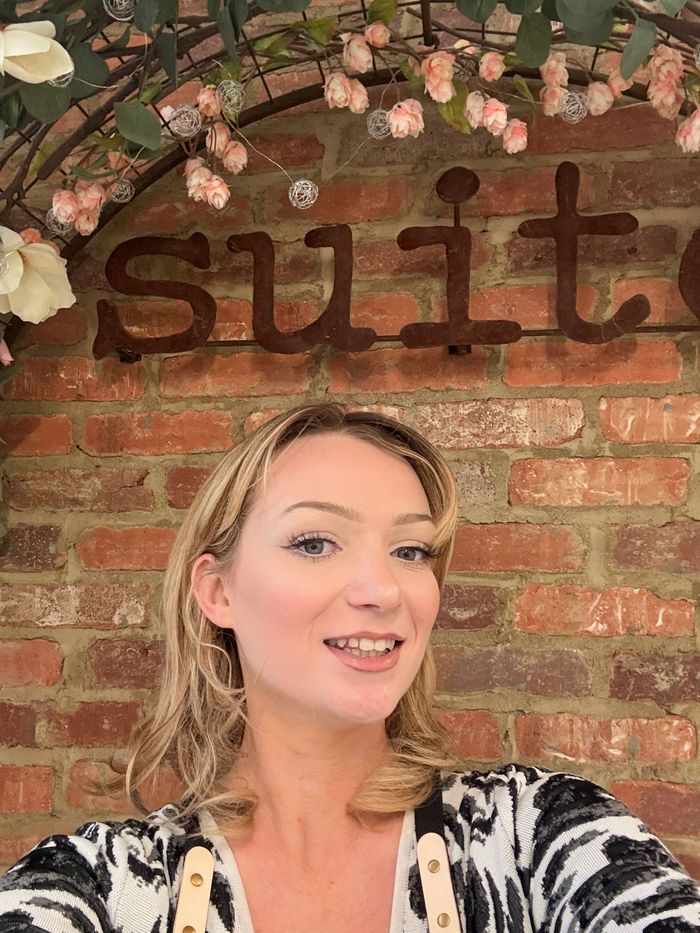A woman in a red dress is taking a selfie in front of a brick wall.