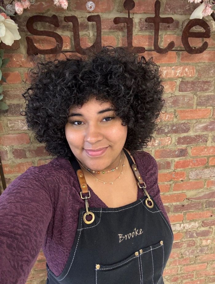 A woman with curly hair is standing in front of a brick wall.