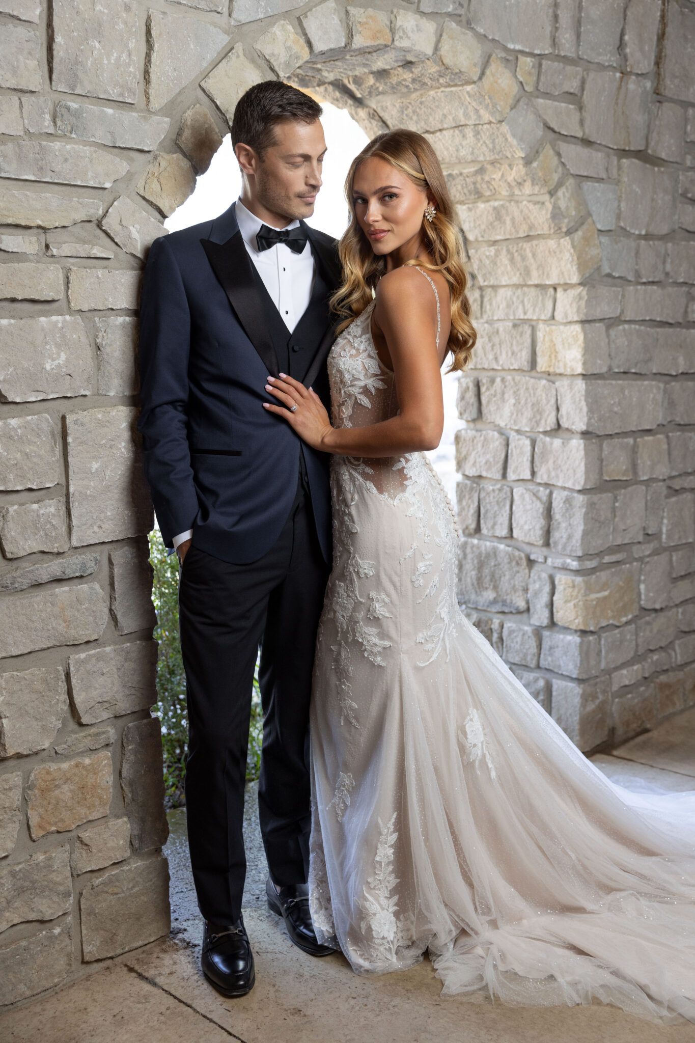 A bride and groom are posing for a picture in front of a stone wall.
