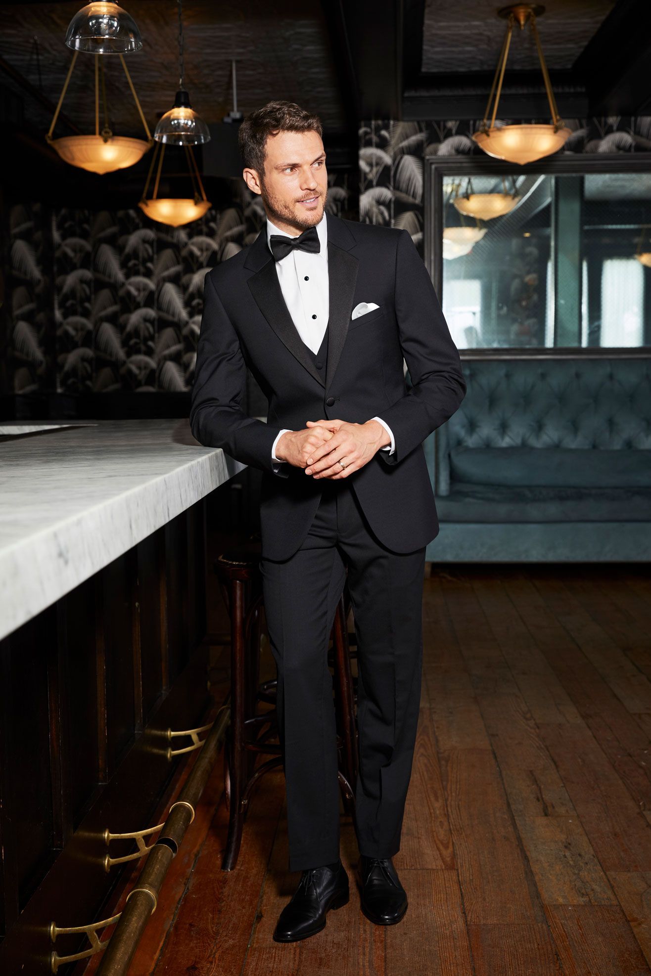 A man in a tuxedo and bow tie is standing in front of a bar.