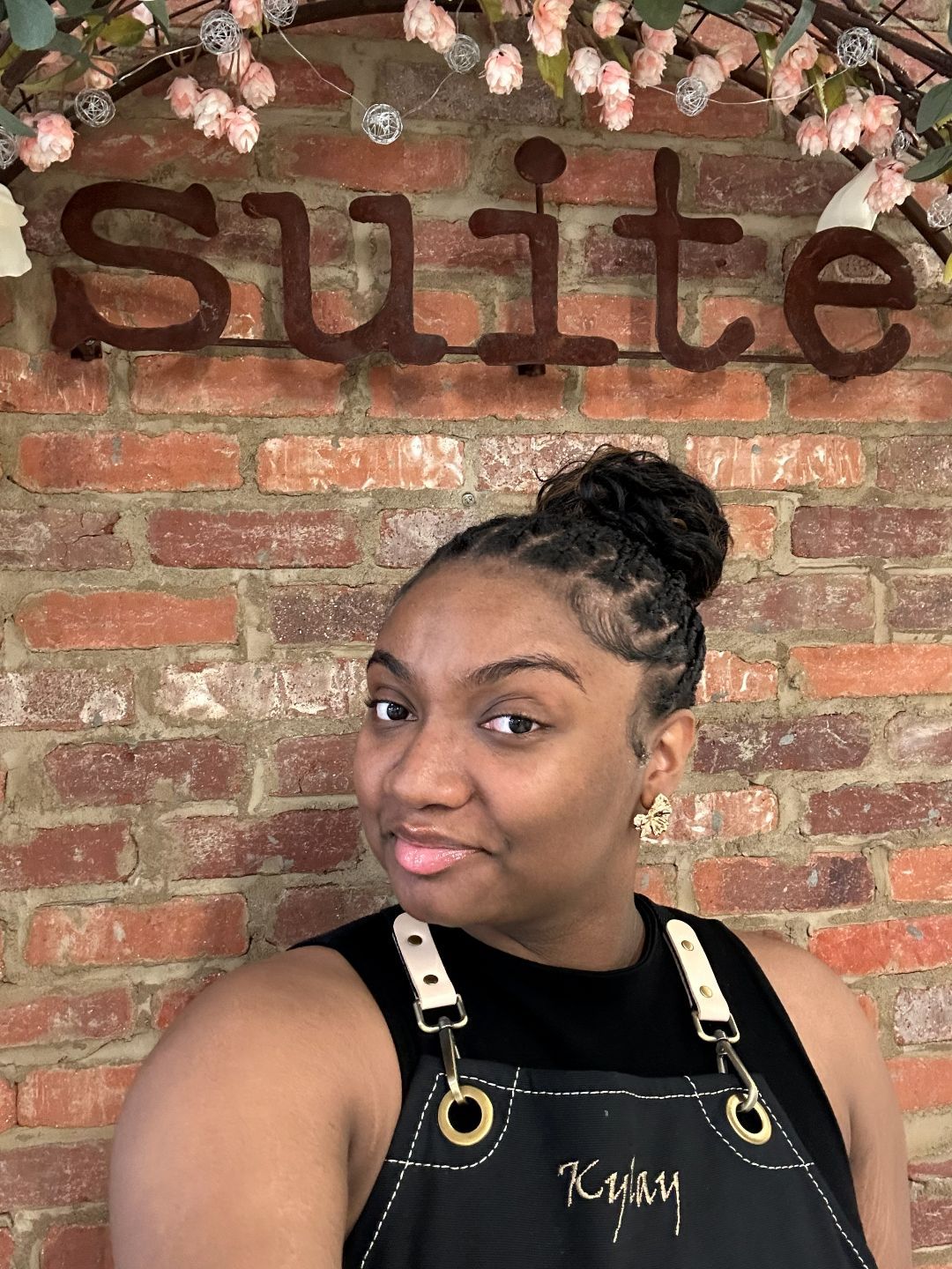 A woman in a red dress is taking a selfie in front of a brick wall.