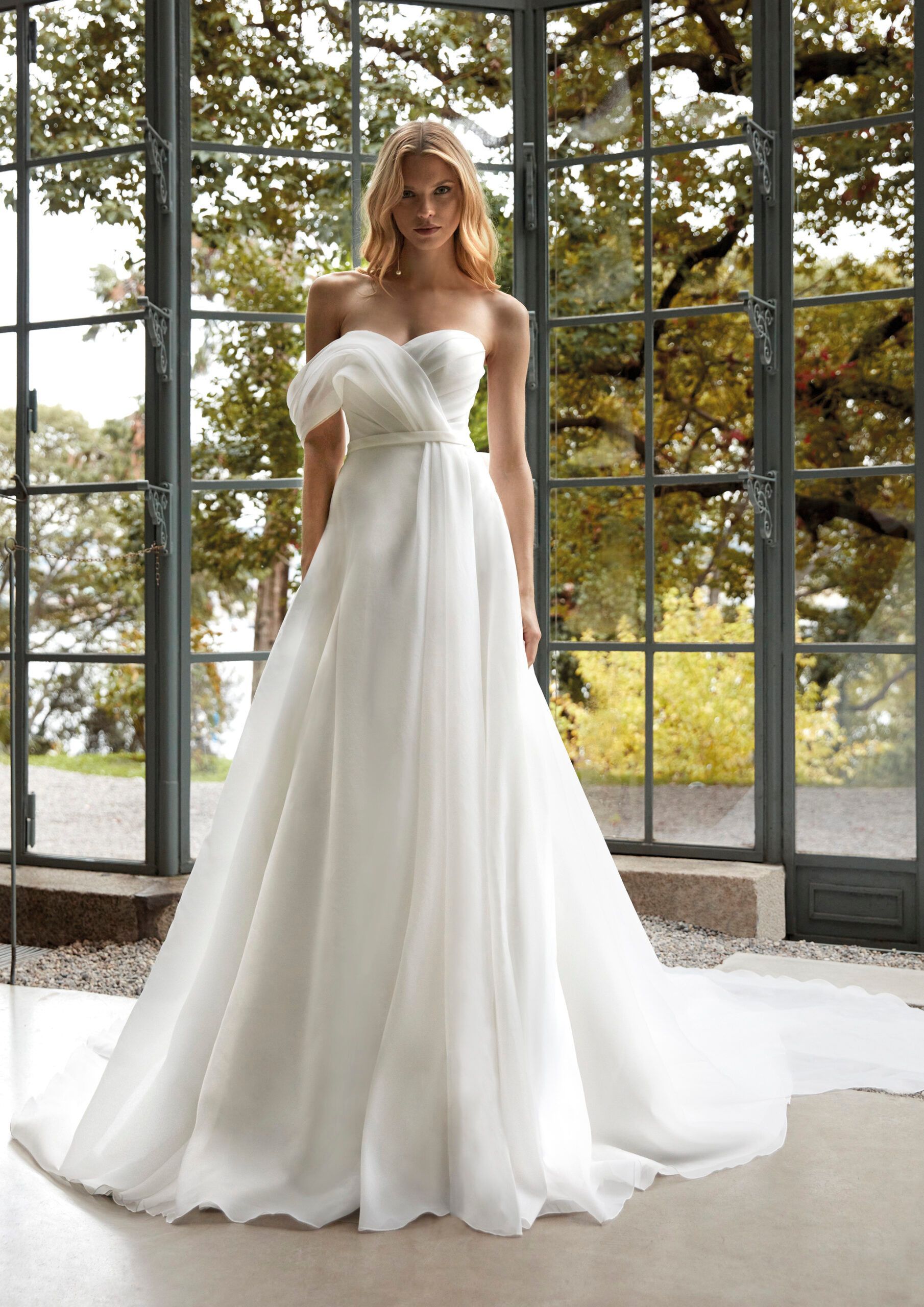 A woman in a white wedding dress is standing in front of a window.