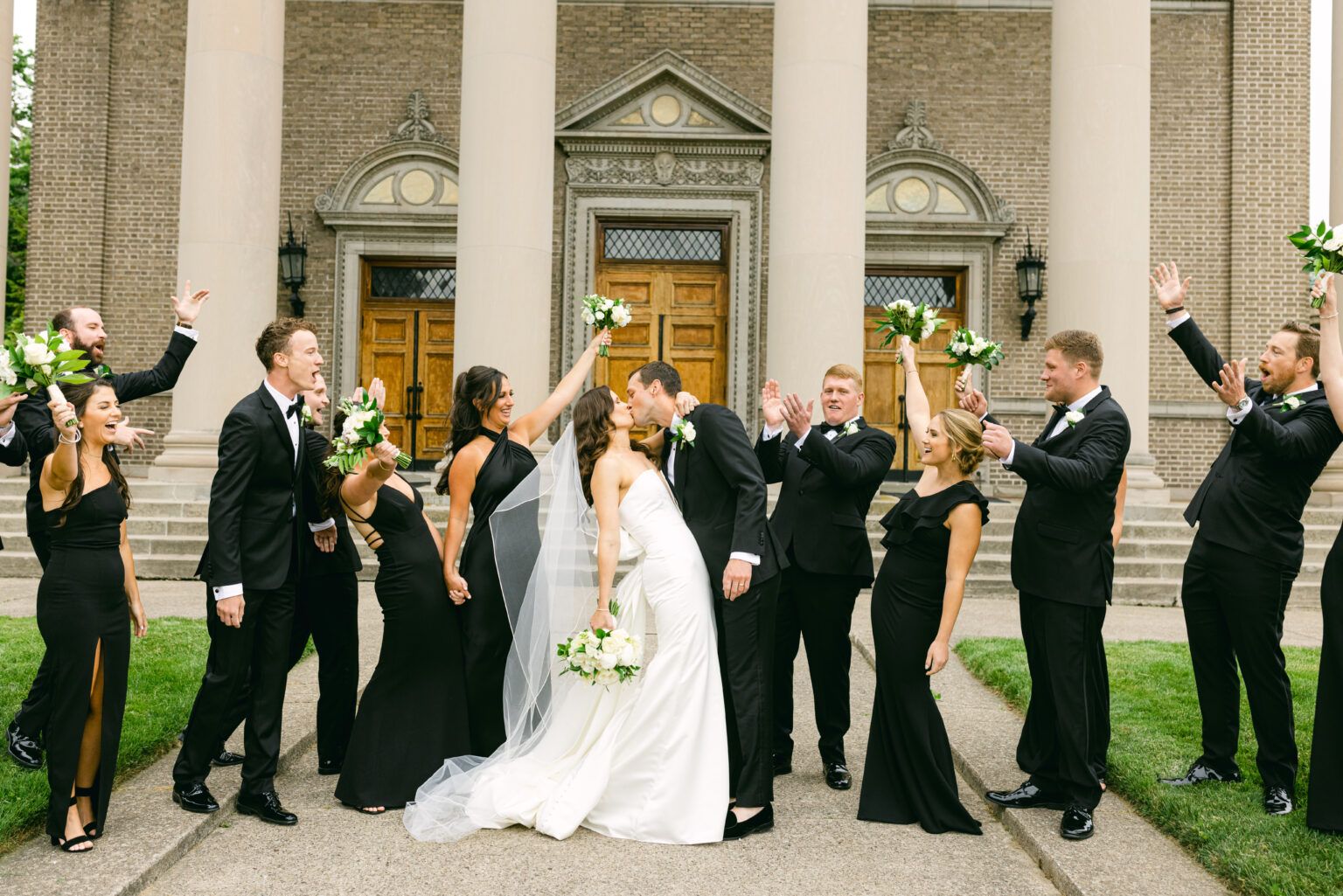 A bride and groom are kissing in front of their wedding party.