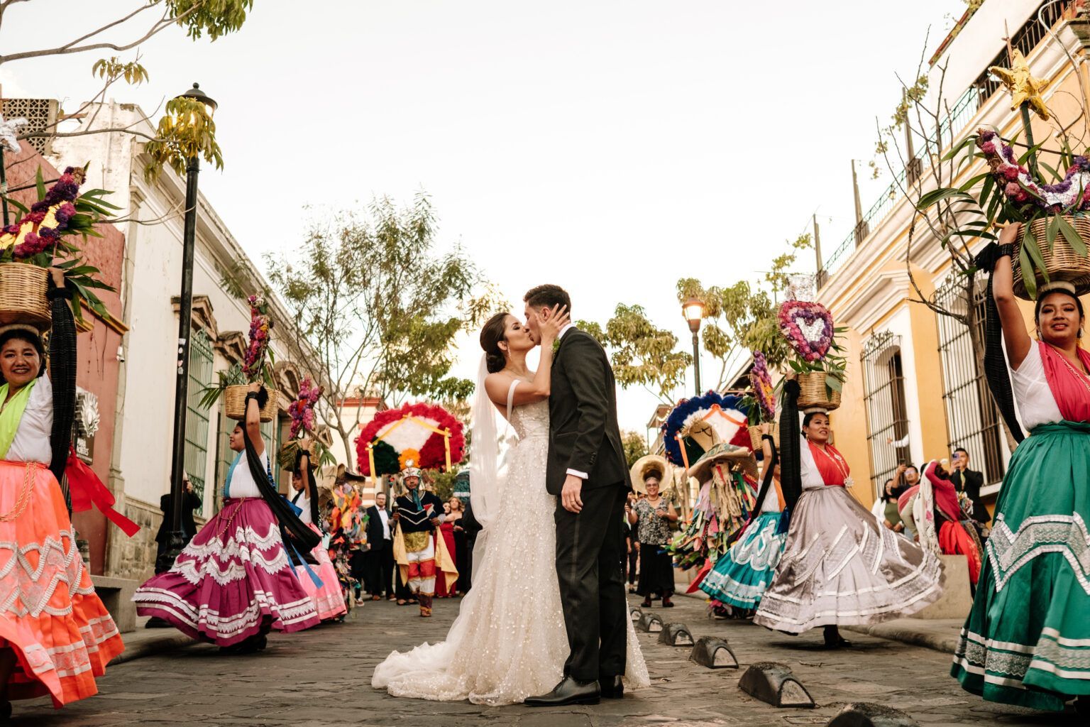 A bride and groom are kissing in front of a group of dancers.