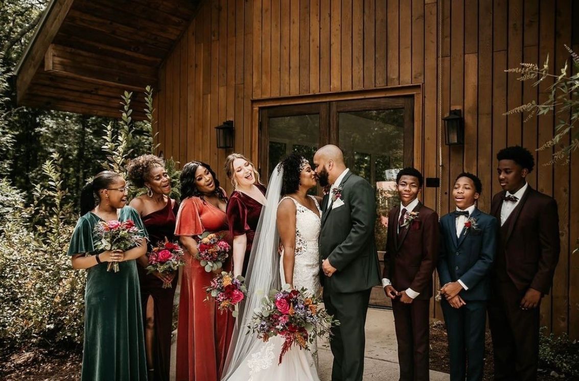 A bride and groom are kissing in front of their wedding party.