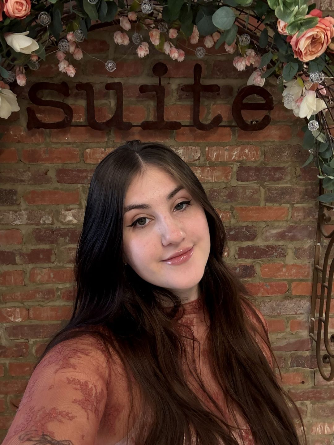 A woman with curly hair is standing in front of a brick wall.