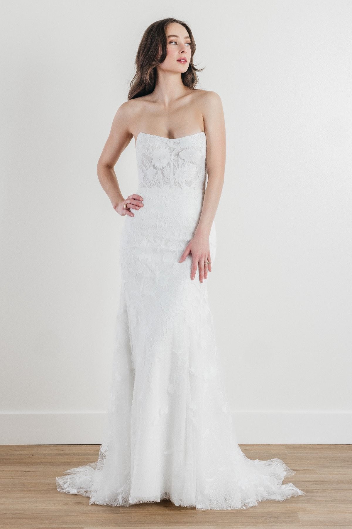 A woman in a white wedding dress is standing on a wooden floor.