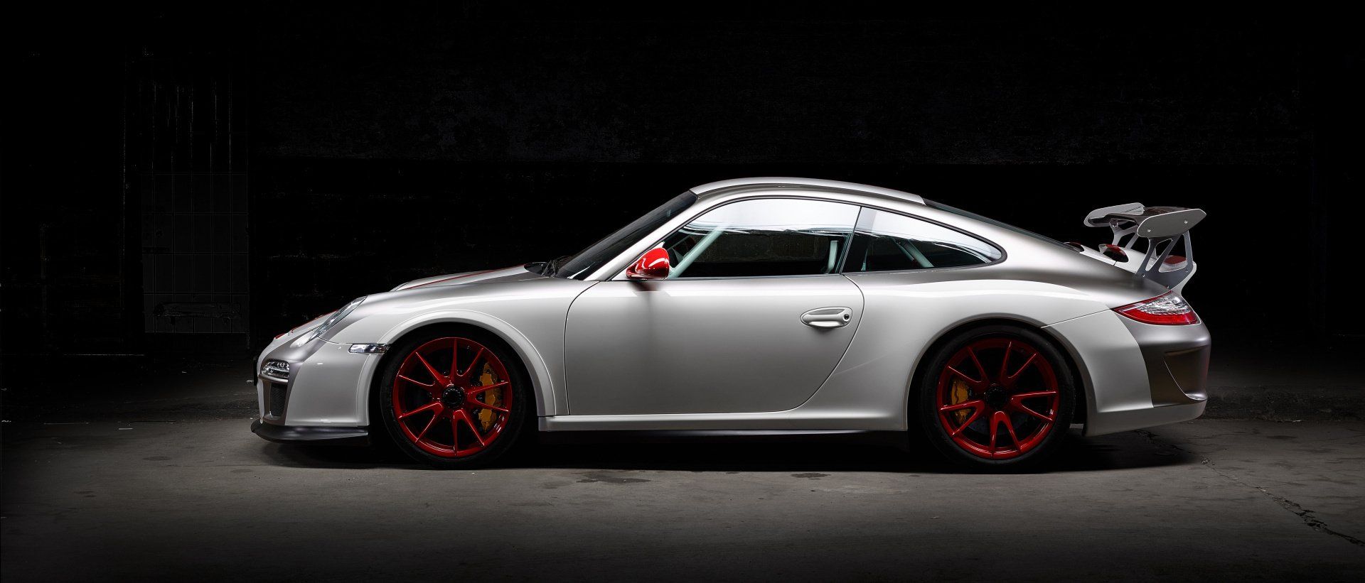 A silver porsche 911 gt3 rs is parked in a dark garage.