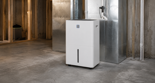 White dehumidifier in a concrete basement next to metal ductwork