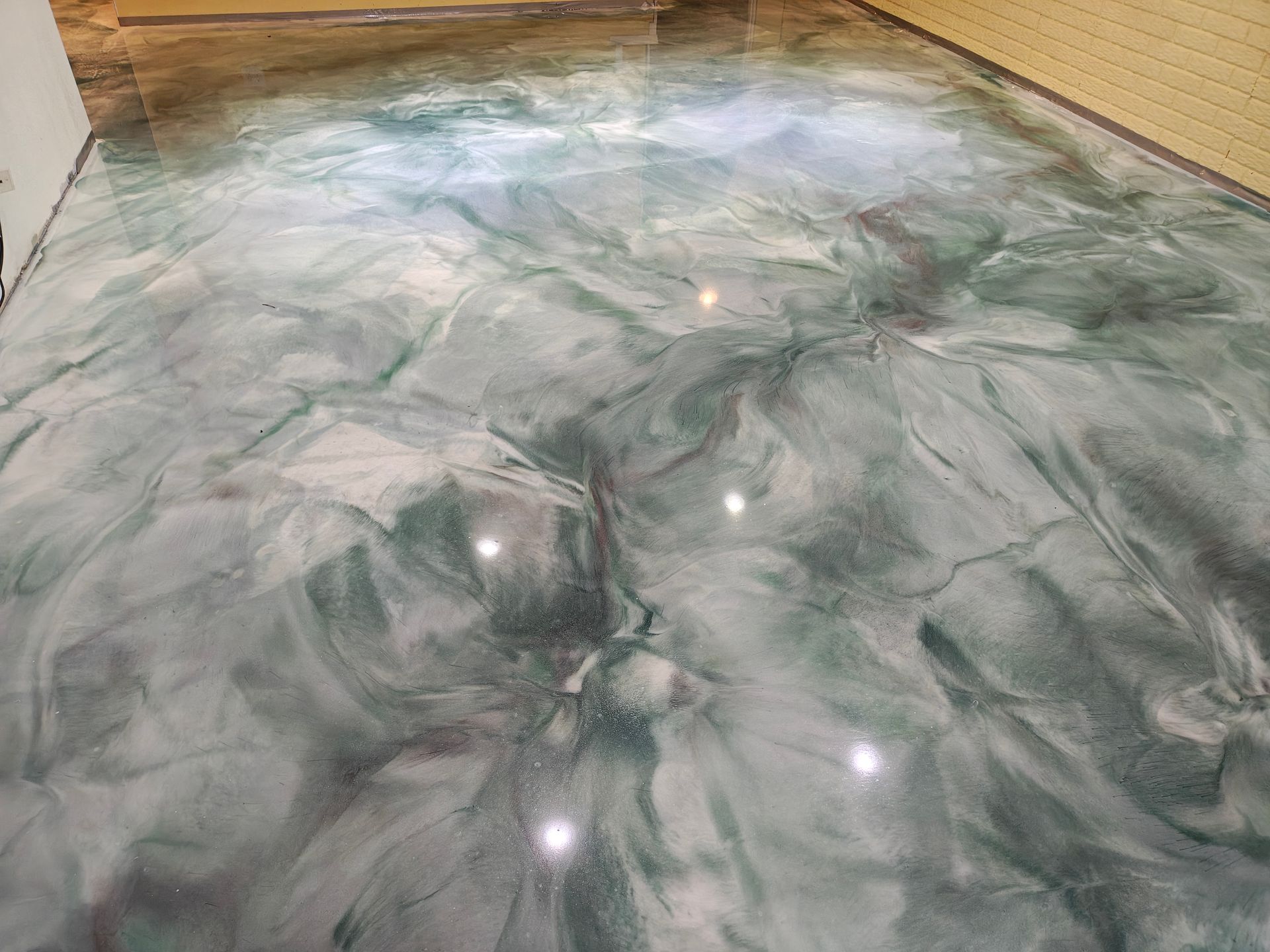 Swirled epoxy floor, green and silver marbled effect, reflecting light.